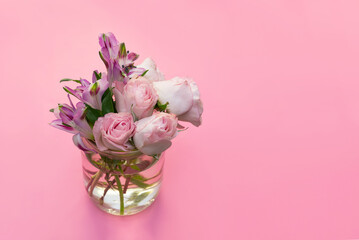 a bouquet of pink flowers in a glass vase with water on a pink background copy space