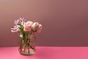 a bouquet of pink flowers in a glass vase with water on a pink background copy space