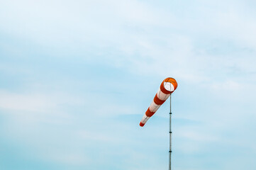 Red and white striped windsock on blue sky background