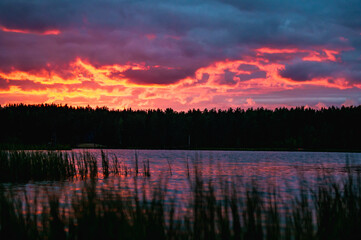 Red sunset with clouds over lake in forest in Russia