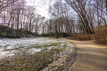 landscape in the park in early spring with melting white snow on a sunny February day