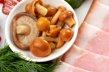 Pickled mushrooms, salted honey mushrooms close-up on a plate with ham.