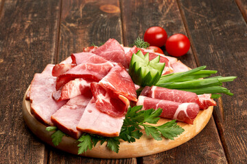 Ham with tomatoes and herbs on a wooden board, wooden background.