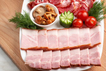 Sliced ham and Italian coppa on a white platter, garnished with herbs and pickled honey mushrooms. Festive table setting for cafe. Close-up.