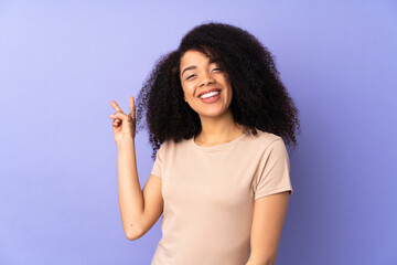 Young african american woman isolated on purple background smiling and showing victory sign