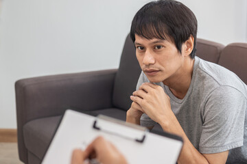 Young asian man, male has mental symptoms which must have been therapy and stress, sitting on couch to consult to psychologist during the session  taking notes to find out how to treat the therapist.