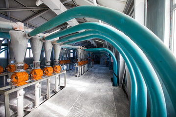 Aktobe region, Kazakhstan - May 06, 2012: Wheat flour production line. Electric motors with cone hoppers and grain mills. Blue plastic pipes.