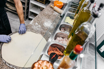 Pizzaiola straightens pizza dough in pizzeria