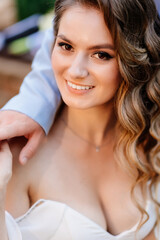 The groom gently hugs shoulders the bride with long curls.