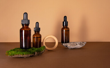 Serum bottles on brown with a beige background. Sustainable lifestyle concept, natural cosmetics. Cosmetic product decorated with moss, stones and wooden ring. Front view, copy space.