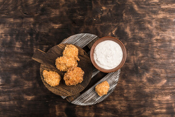 Obraz na płótnie Canvas Chicken nuggets on a wooden board with white cream sauce on a dark background.