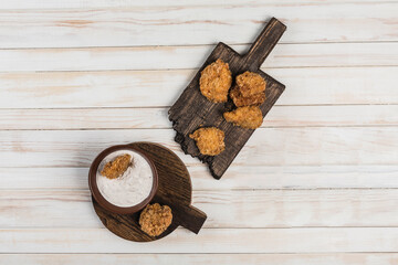 Chicken nuggets on a wooden board with white cream sauce on a light background.