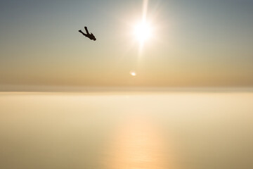 Skydiver flies over the sea at sunset.