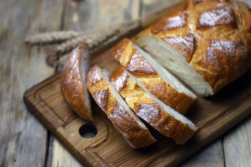 Fresh wheat bread slices on a wooden surface. Ears of wheat. Rustic style.