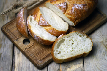 Fresh wheat bread slices on a wooden surface. Ears of wheat. Rustic style.
