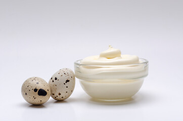 Closeup of two whole quail eggs, glass bow full of mayonnaise on the white surface