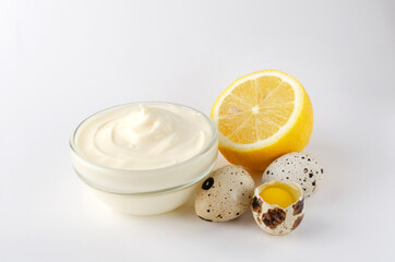 Closeup of glass bowl of delicious mayonnaise and juicy lemon, quail eggs on the white background
