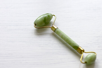 Green jade face roller, natural stone for skin care, on white backdrop. Tool for facial lifting massage, trendy therapy  © Olga