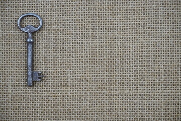 Bodegón minimalista de aspecto rústico que presenta una llave antigua reposando a la izquierda sobre un paño de arpillera.