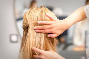 Fototapeta premium Close up of female hairdresser styling blonde hair of a young woman in a beauty salon
