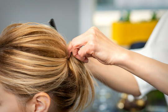 Close up of female hairdresser styling blonde hair of a young woman in a beauty salon