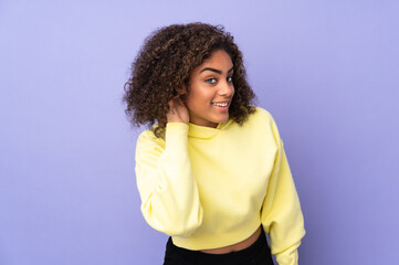 Young African American woman isolated on background listening to something by putting hand on the ear