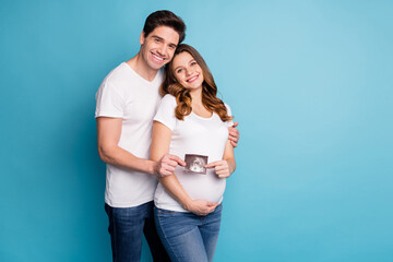 Photo of young cheerful positive smiling happy family hold ultrasound photo of baby isolated on blue color background