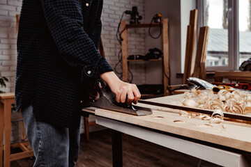 Carpenter's hands planing a plank of wood with a hand plane