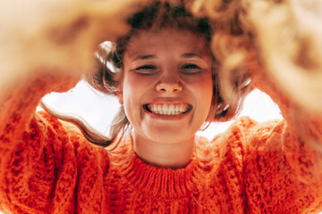 Closeup of a candid gorgeous young woman wearing a knitted orange sweater smiling broadly and...