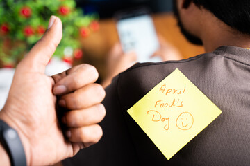 Selective focus on t-shirt, Pasting aprils fools day sticker on young mans shoulder while busy on...