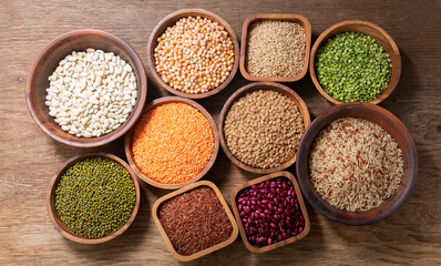 bowls of legumes, lentils, chickpeas, beans, rice and cereals on wooden background