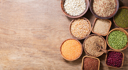bowls of legumes, lentils, chickpeas, beans, rice and cereals on wooden background