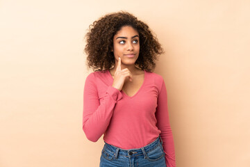 Young African American woman isolated on beige background thinking an idea while looking up