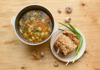 cauldron of soup and baked meat on a plate, green onion and garlic on wooden background, home cooking