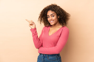 Young African American woman isolated on beige background pointing finger to the side