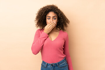 Young African American woman isolated on beige background covering mouth with hand