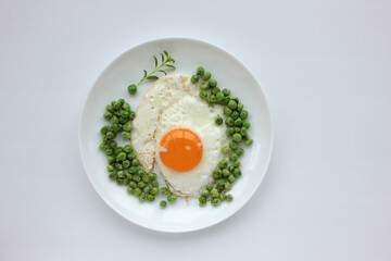 Fried egg with green peas on a white plate on white table background. Healthy breakfast or brunch concept. Sunny side up served with vegetables on a dish. Top view