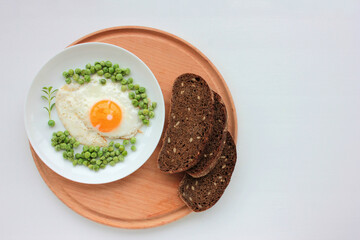 Fried egg with green peas on a white plate and rye bread on white table background. Healthy breakfast or brunch concept. Sunny side up served with vegetables on a dish. Top view. 
