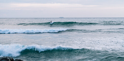 Surfer na fali, na tle oceanu, skał i wzburzonej wody. © insomniafoto