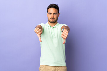 Fototapeta premium Young handsome man isolated on purple background showing thumb down with two hands