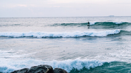 Surfer na fali, na tle oceanu, skał i wzburzonej wody. © insomniafoto