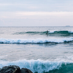 Surfer na fali, na tle oceanu, skał i wzburzonej wody. © insomniafoto