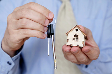 Real estate agent, apartment keys and wooden house in male hands. Man in office clothes with house model, purchase or rental home