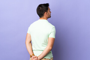 Young handsome man isolated on purple background in back position and looking back
