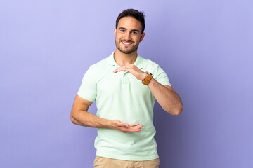 Young handsome man isolated on purple background holding copyspace imaginary on the palm to insert an ad