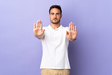 Fototapeta premium Young handsome man isolated on purple background making stop gesture and disappointed