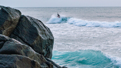 Surfer na fali, na tle oceanu, skał i wzburzonej wody.