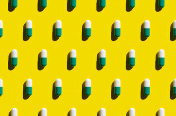 White and green pill capsule pattern on a yellow background. Hard shadows.