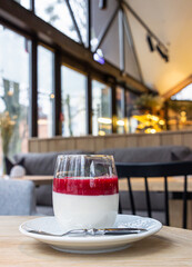 Delicious Italian dessert panna cotta with red berry sauce on wooden table, cafe interior background.