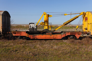 Fototapeta na wymiar Old yellow cargo crane wagon on abandoned train tracks in the field